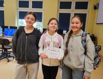 Obraz trójki szczęśliwych uczniów w pokoju komputerowym, z których jeden trzyma certyfikat przejścia gry o cyberbezpieczeństwie.