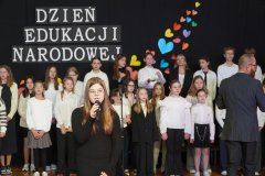 Dziewczynka śpiewa do mikrofonu. W tle widnieje chór.