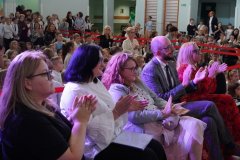 W pierwszym rzędzie siedzą: Dyrektor Szkoły, Wicedyrektorzy oraz Przedstawiciele Rady Rodziców. W tle widać Uczniów siedzących na podłodze.