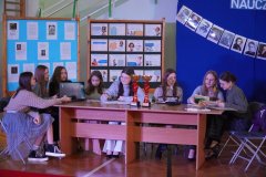 Na tle tablic informacyjnych z gazetą o Dniu Nauczyciela, przy stole siedzi osiem uczennic odgrywających rolę nauczycieli. Dziewczyny opowiadają o trudach pracy w zawodzie pedagogów.
