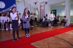 Chór TuTu z zespołem muzycznym i solistki śpiewające piosenkę.