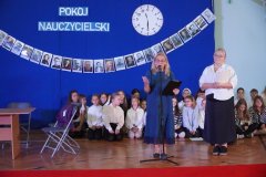 Na tle granatowej dekoracji z napisem pokój nauczycielski, Panie Dyrektor Marlena Błachowicz i Monika Przemyłska składają życzenia nauczycielom i pracownikom szkoły.