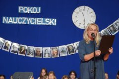 Na tle granatowej dekoracji z napisem pokój nauczycielski, Pani Dyrektor Marlena Błachowicz wyczytuje kolejnych nauczycieli, który otrzymali nagrody Prezydenta i Dyrektora.