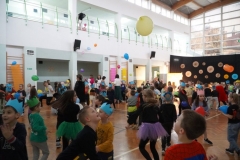 Duża grupa dzieci na sali gimnastycznej łapie balony podczas balu.