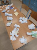 Na stole leży dużo złożonych karteczek z zapisanymi nazwiskami, które są segregowane i odczytywane podczas podliczania wyników akcji Samorządu Uczniowskiego z okazji Dnia Kobiet.