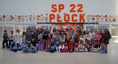 Liczna grupa uczniów oraz nauczycieli SP 22 w Płocku podczas Dnia Piżamy. Wspólne zdjęcie wykonane na forum szkoły, uczestnicy ubrani w piżamy i szlafroki. 
