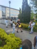Na zdjęciu widać grupę Dzieci znajdującą się na zewnątrz budynku szkolnego. Trzymają One w rękach kolorowe plakaty dotyczące ochrony środowiska i rozmawiają ze sobą na ich temat. 