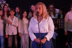 Kobieta w białej bluzce i granatowej spódnicy przemawia do mikrofonu 