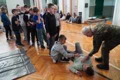 Grupka Uczniów czeka, aby przećwiczyć umiejętność ułożenia poszkodowanego w pozycji bezpiecznej. Nad prawidłowym wykonaniem tych czynności czuwa Prowadząca.