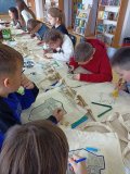 długi stół, przy którym siedzi grupa uczniów zajęta ozdabianiem flamastrami toreb bawełnianych