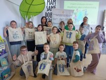 zdjęcie grupowe - klasa 3a z wychowawcami oraz prowadzącą warsztaty pozuje do wspólnego zdjęcia, w rękach prezentują pokolorowane torby bawełniane, w tle baner z napisem „Bądźmy eko z biblioteką”