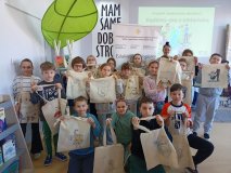 zdjęcie grupowe - klasa 3b z prowadzącą warsztaty pozuje do wspólnego zdjęcia, w rękach prezentują pokolorowane torby bawełniane, w tle baner z napisem „Bądźmy eko z biblioteką”
