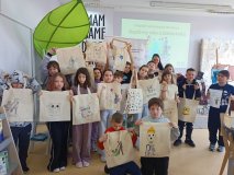 zdjęcie grupowe - klasa 3d z prowadzącą warsztaty pozuje do wspólnego zdjęcia, w rękach prezentują pokolorowane torby bawełniane, w tle baner z napisem „Bądźmy eko z biblioteką”