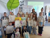 zdjęcie grupowe - klasa 3e z wychowawcami oraz z prowadzącą warsztaty pozuje do wspólnego zdjęcia, w rękach prezentują pokolorowane torby bawełniane, w tle baner z napisem „Bądźmy eko z biblioteką”