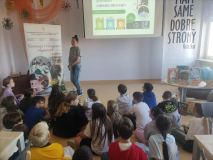 Grupa dzieci siedzi na podłodze i z uwagą słucha edukatorki z Przedsiębiorstwa Gospodarowania Odpadami w Płocku.