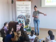 Grupa dzieci siedzi na podłodze i z uwagą słucha edukatorki z Przedsiębiorstwa Gospodarowania Odpadami w Płocku.