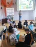 Grupa dzieci siedzi na podłodze i z uwagą słucha edukatorki z Przedsiębiorstwa Gospodarowania Odpadami w Płocku.