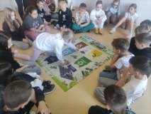 Grupa dzieci siedzi wokół planszy i gra w ekosegregację.