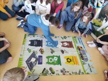 Grupa dzieci siedzi wokół planszy i gra w ekosegregację.