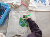 Dziecko przy stole maluje Ziemię na bawełnianej torbie.