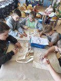 Grupa dzieci przy stołach maluje bawełniane torby.