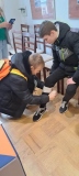Dwóch chłopców, jeden z nich opatruje bandażem nogę koledze.