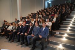 Grupa kobiet i mężczyzn siedzących w auli widowiskowej.