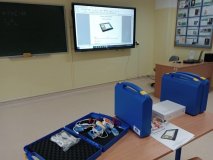 foto_1 Sala lekcyjna: na ławce nowoczesne zestawy edukacyjne do eksperymentów naukowych – widoczne niebieskie walizki z czujnikami i akcesoriami oraz podręcznik z doświadczeniami z fizyki, w tle tablica interaktywna z wyświetlaną nazwą zajęć "Cyfrowe Laboratorium Młodego Einsteina" oraz tradycyjna tablica