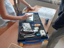 foto_10  Na ławce znajduje się nowoczesny zestaw edukacyjny do eksperymentów naukowych – widoczna jest niebieska walizka z czujnikami i akcesoriami oraz tablet podłączony do dalmierza- dwie uczennice dokonują pomiarów ruchu