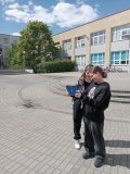 foto_11 Dwie uczennice w słoneczny dzień na placu przed szkołą dokonują czujnikiem wbudowanym w tablet pomiaru poziomu promieniowania UV