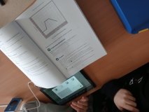foto_7 Na ławce szkolnej znajduje się tablet z uruchomionym oprogramowaniem do rysowania wykresów ruchu oraz podręcznika otwarty na stronie z instrukcją doświadczenia