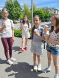 Grupka uśmiechniętych uczennic z lodami w dłoniach. W tle nasłonecznione, bujne drzewa i osiedlowe zabudowania.