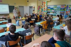 Sala lekcyjna. Uczniowie klasy czwartej siedząc w ławkach słuchają mini – wykładu o bezpieczeństwie w sieci: „Jak się nie zaplątać w sieci?”. Zajęcia prowadzi - Pani Marlena Szymczak, profilaktyk z Komendy Miejskiej Policji w Płocku.