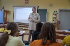 Sala lekcyjna. Uczniowie klasy czwartej siedząc w ławkach oglądają prezentację filmową na ekranie o bezpieczeństwie w sieci: „Jak się nie zaplątać w sieci?”. Zajęcia prowadzi - Pani Marlena Szymczak, profilaktyk z Komendy Miejskiej Policji w Płocku.