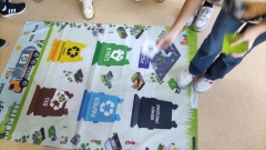 Dzieci uczą się przy użyciu maty edukacyjnej, jak segregować odpady.