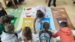 Dzieci układają mega puzzle tematycznie związane z segregacją odpadów.