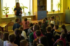 Świetlica szkolna. Uczniowie klas pierwszych siedząc na dywanie, słuchają i dyskutują na trudne tematy związane z substancjami uzależniającymi. Zajęcia prowadzi przedstawiciel Spółki, Starszy Laborant, Pani Aleksandra Pokorska.