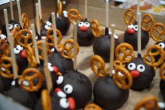 Zbliżenie na świąteczne słodkości typu cake pops. Czekoladowe kuleczki na patykach udekorowane są tak, by przypominały renifery – mają poroża z precli, oczy z cukrowych koralików i czerwone nosy.