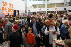 Tłum uczestników „Mikołajkowego Kiermaszu Rozmaitości” na forum Szkoły Podstawowej nr 22 w Płocku. W tle widnieje duży napis „SP 22 PŁOCK”, a na pierwszym planie dzieci i dorośli przeglądają stoiska z zabawkami, rękodziełem i biżuterią.