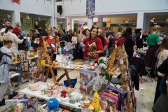 Tłum uczestników „Mikołajkowego Kiermaszu Rozmaitości” na forum Szkoły Podstawowej nr 22 w Płocku. W tle widnieje duży napis „SP 22 PŁOCK”, a na pierwszym planie dzieci i dorośli przeglądają stoiska z zabawkami, rękodziełem i biżuterią.