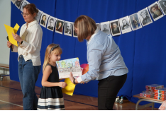 Jeden nauczyciel wyczytuje laureata konkursu plastycznego w kategorii klas pierwszych. Drugi nauczyciel wręcza uczennicy z klasy pierwszej dyplom i nagrodę. 