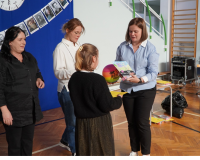 Jeden nauczyciel wyczytuje laureata konkursu plastycznego w kategorii klas trzecich. Drugi nauczyciel wręcza uczennicy klasy trzeciej dyplom i nagrodę.