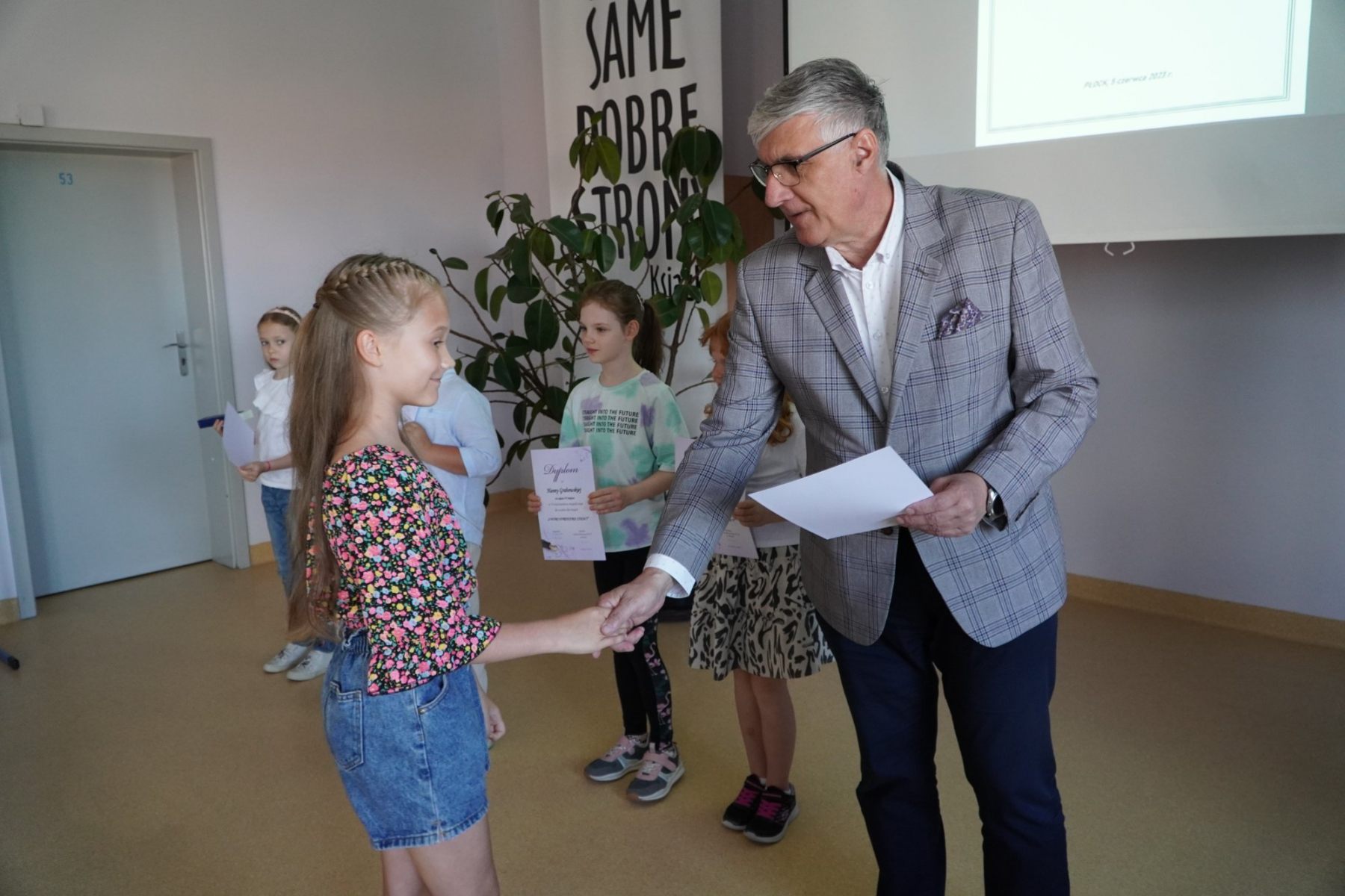 Pan Dyrektor wręcza dyplom za udział w Konkursie Ortograficznym uczennicy klasy drugiej. Na dyplomie widnieje wieczne pióro, symbol konkursu.
