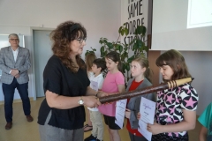 Pani Anna Markowska za pomocą dużego, drewnianego pióra pasuje uczniów na „Mistrza Ortografii”.