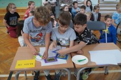Trzech Uczniów klasy 3b siedzi przy stoliku i dopasowuje zdjęcia zwierząt do zapisu kolejnych zagadek. Za Chłopcami siedzą pozostali Członkowie zespołu. 