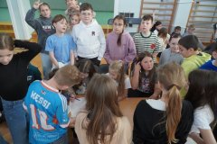 Trzy Uczennice klasy 3e siedzą przy stoliku i rozwiązują zadanie konkursowe. Dziewczynki są wspomagane przez  stojących obok pozostałych Członków zespołu.