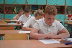 Kilku uczniów piszących konkurs siedząc w ławkach.
