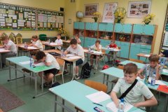 Sala lekcyjna w której uczniowie siedzą pojedynczo przy ławkach pisząc konkurs.