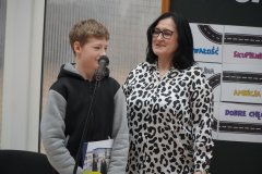 Kobieta - pani wicedyrektor szkoły oraz uczeń w szarej bluzie stoją uśmiechnięci przed mikrofonem. W tle kręta droga do sukcesu.