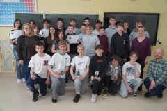 W sali lekcyjnej na tle zielonej tablicy szkolnej znajduje się grupa uczestników konkursu- uczniowie klas 7, po lewej stronie grupy jest Pani Wicedyrektor, a po prawej nauczycielka fizyki oraz obok niej, kucając- nauczyciel chemii. Uczniowie trzymają w rękach tematyczne dyplomy, nagrody książkowe oraz zakładki do książek. Wszyscy w bardzo pogodnym nastroju.